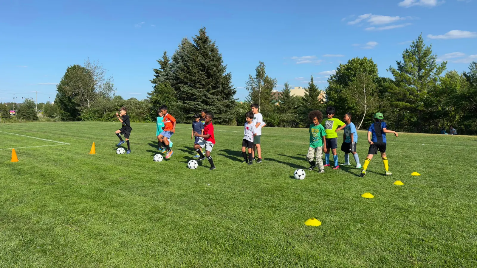 Children and youth completing a soccer dribbling drill on a sunny field.