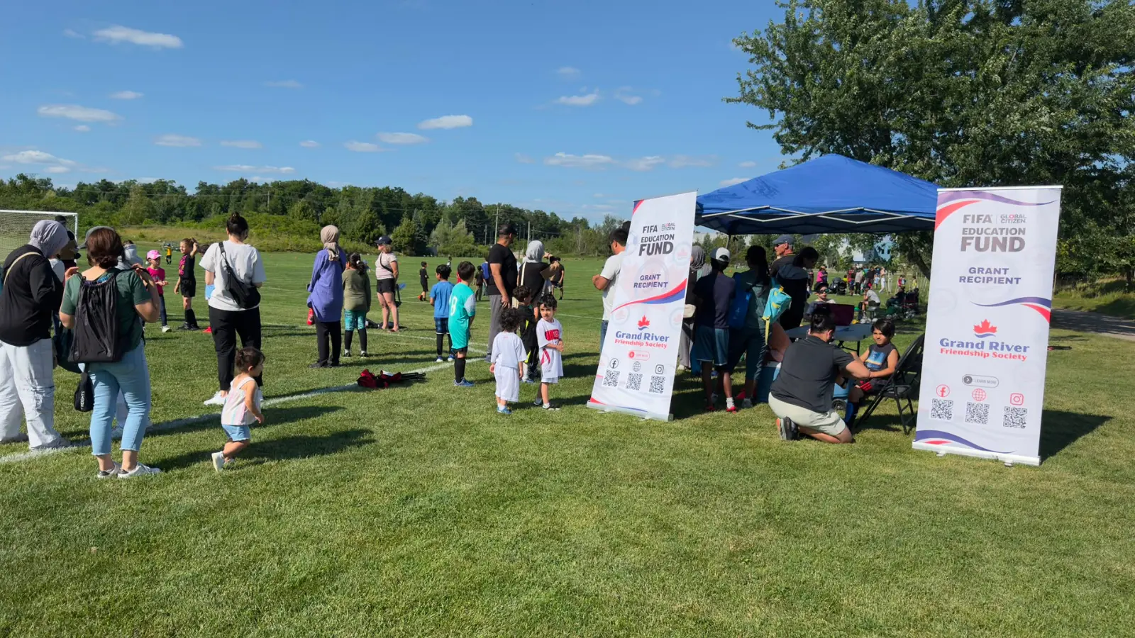 Families checking in beside GRFS and FIFA Education Fund banners at summer soccer training.