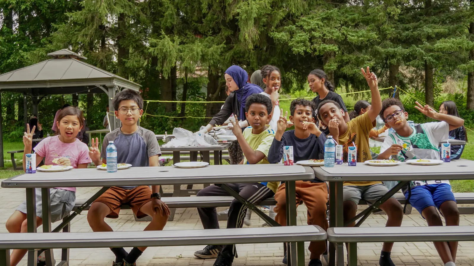 Kids To Camp 2026 participants sharing a meal and friendship at outdoor picnic tables.