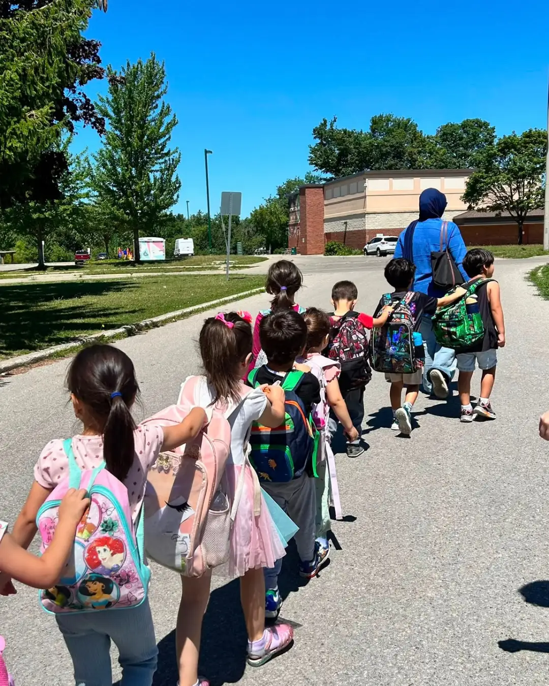 Children with backpacks walking in a line behind a mentor outdoors at GRFS Summer School 2026