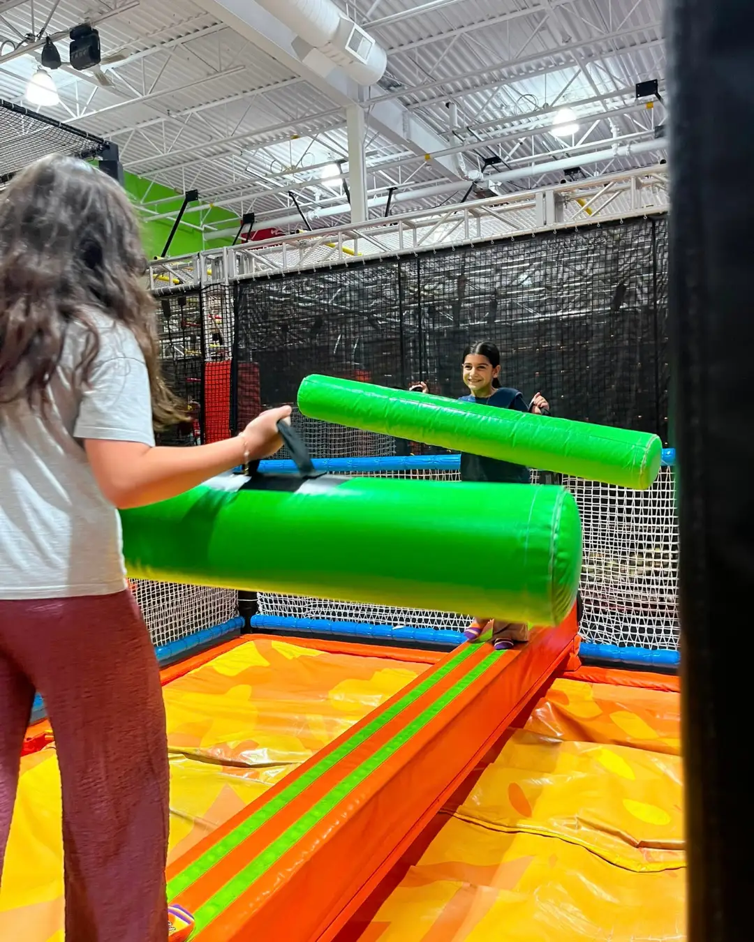 Children balancing with foam jousting poles at an indoor activity centre at GRFS Summer School 2026
