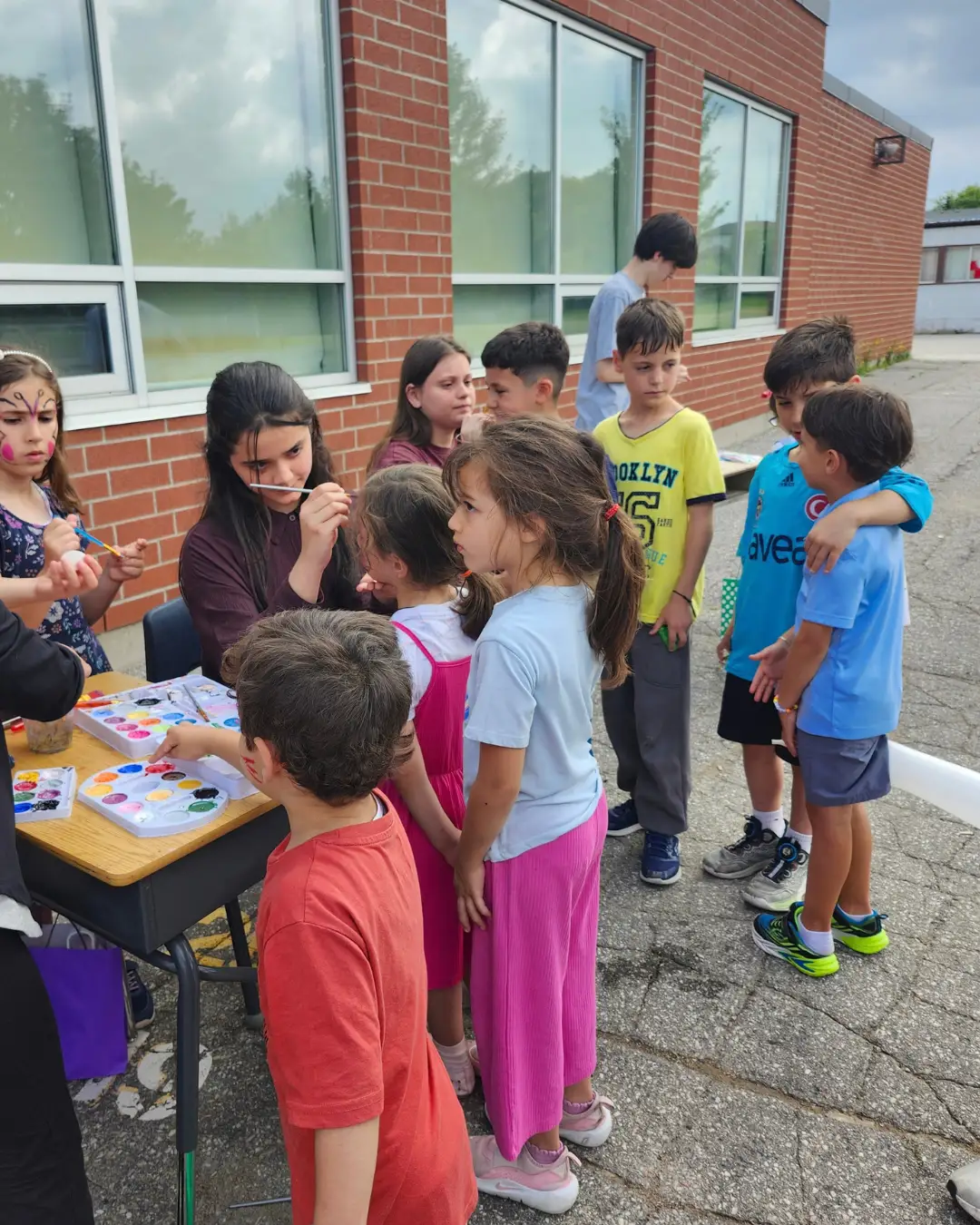 Children gathering around an outdoor face-painting station at GRFS Summer School 2026