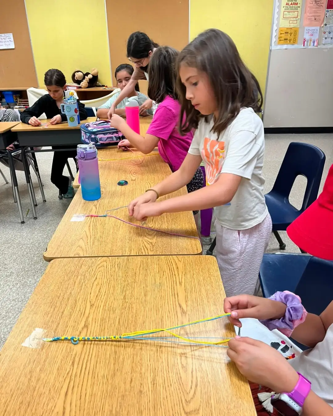 Children making colourful friendship bracelets at classroom desks at GRFS Summer School 2026