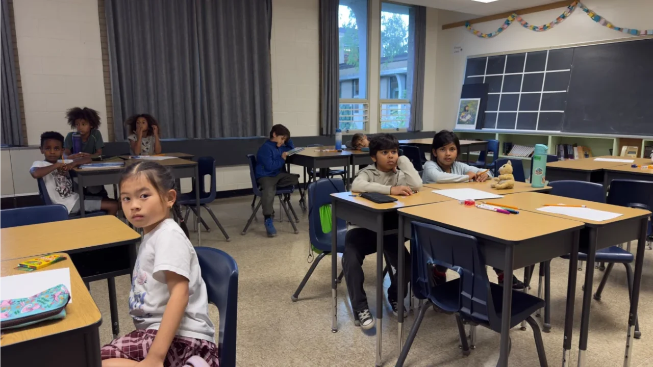 Children seated at grouped desks with worksheets and pencils during GRFS in-person learning sessions.