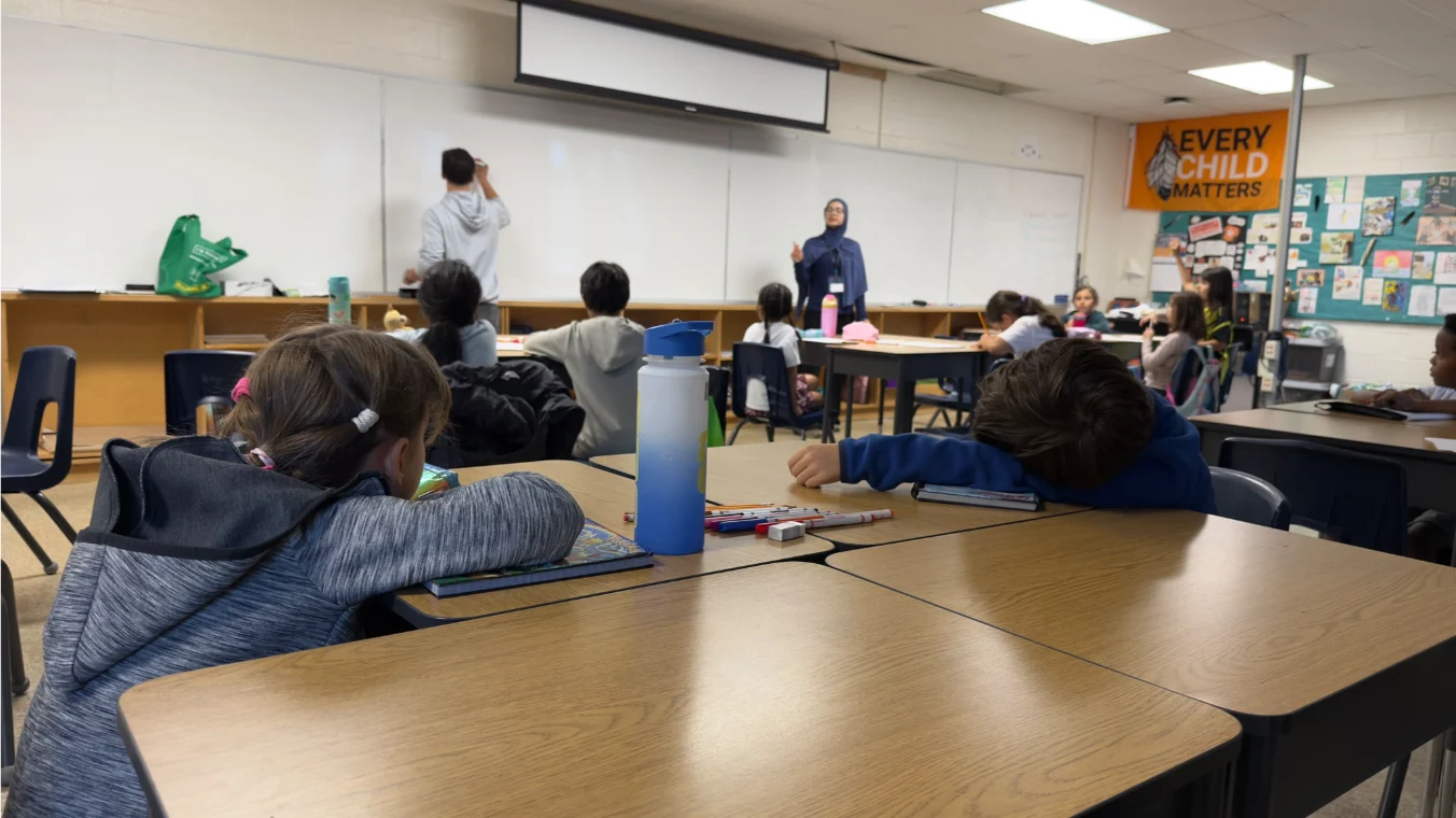 A student working at the whiteboard while classmates and an instructor take part in a learning activity.